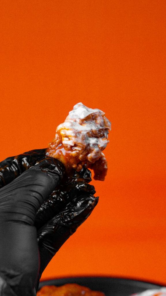 hand in black gloves holding chicken piece covered in sauce
