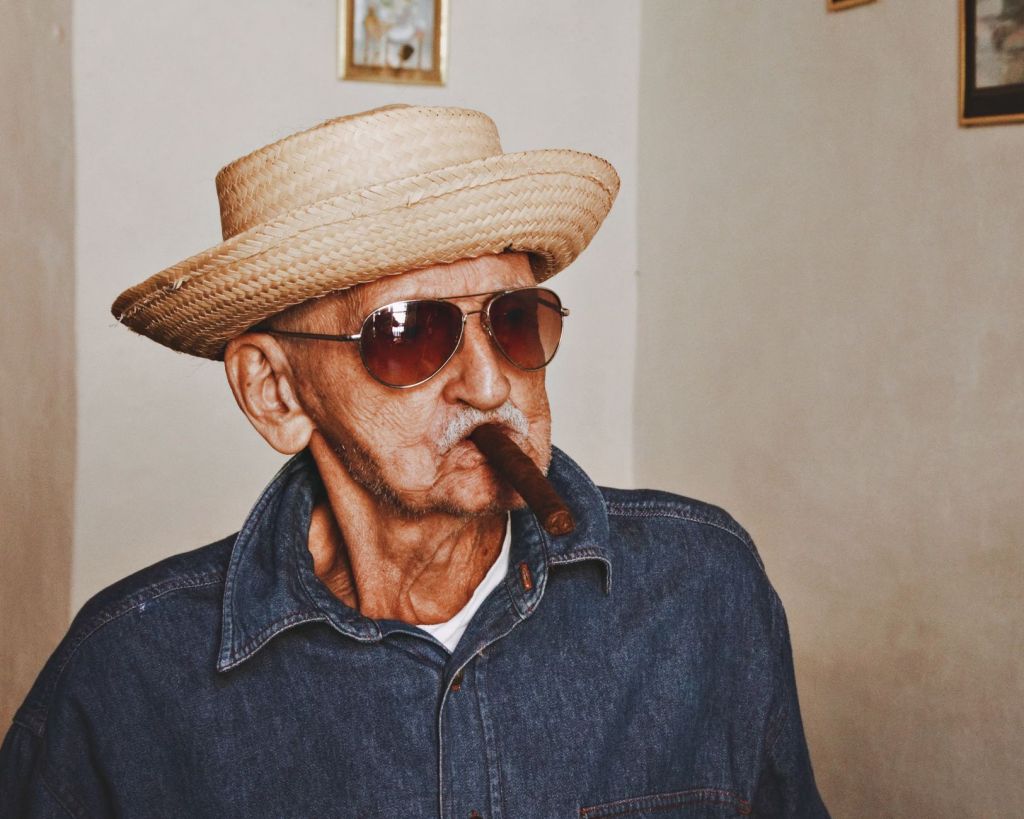 elderly man in a straw hat and sunglasses smoking a cigar